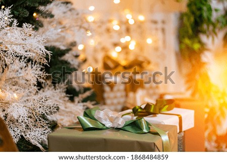 Gifts boxes lie under Christmas tree in interior, bokeh illuminated in background.