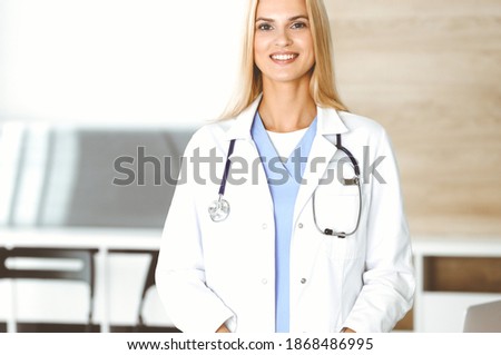Woman-doctor at work in clinic excited and happy of her profession. Blond female physician is smiling while using tablet computer. Medicine concept