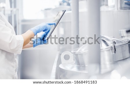 Operator uses tablet computer to check quality and temperature of yeast fermentation in tanker hops and malt, beer production.