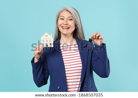 Funny gray-haired business woman in blue suit posing isolated on pastel blue wall background studio portrait. Achievement career wealth business concept. Mock up copy space. Hold house, bunch of keys