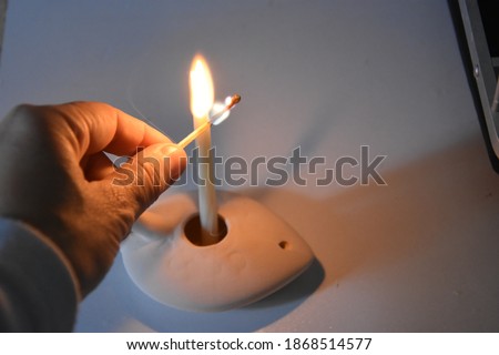 hand lights a white taper in a ceramic stand, Hanukkah light holiday evening. High quality photo Royalty-Free Stock Photo #1868514577