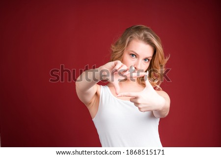 Blond woman in tank top represents a photographer on the red background.
