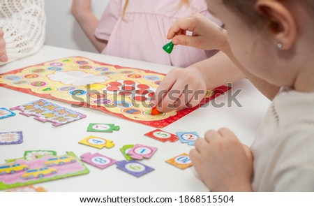 A kindergarten teacher plays a board game with two little girls. Mom plays with little daughters Royalty-Free Stock Photo #1868515504