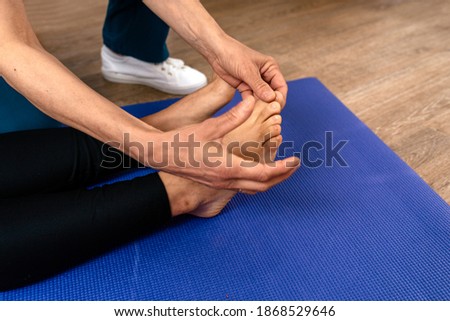 Stock photo of physiotherapist giving feet massage to patient lying in mat.