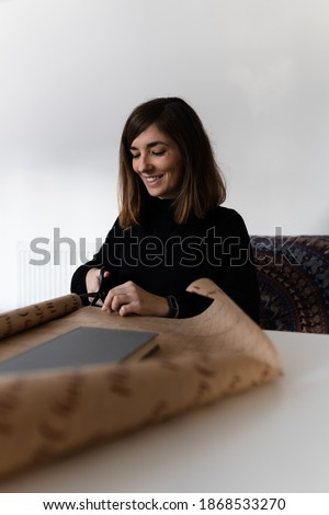 Attractive young female wrapping a book with a recyclable wrapping paper. During Christmas, tons of paper are wasted due to wrapping of the different gifts.