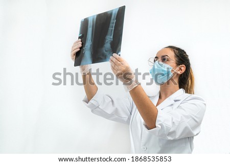 Young doctor with a mask examining a leg X-ray on a white background