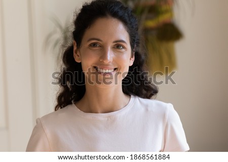 Head shot portrait smiling attractive woman looking at camera, beautiful young female with toothy smile standing at home, posing for profile picture, happy blogger recording vlog, video call