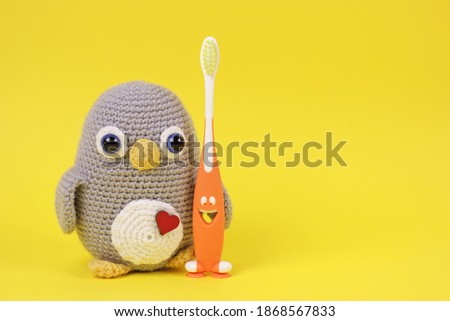 Pretty baby scene with handmade knitted toy.Crochet Amigurumi penguin toy with toothbrush on yellow background.Great for small businesses, children bloggers, social network pages, stores, websites.