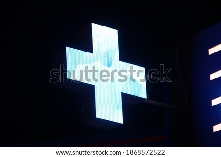 Glowing pixel cross of LED lamps on black background. Blue cross symbol of health, medicine, self-care. Stock photo with empty space for text and design.