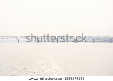 railroad bridge over a wide river and the silhouette of a distant city behind it in the morning haze