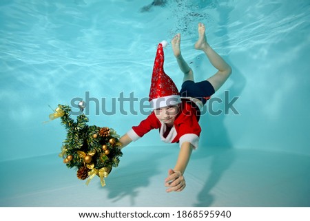Portrait of a boy underwater in a Santa Claus costume in the pool. He is holding a Christmas tree. Outdoor activity. Healthy lifestyle. A swimming school. The concept of the celebration