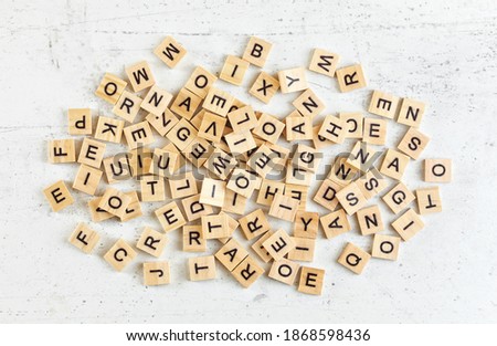 Pile of wooden tiles with various letters scattered on white stone like board, view from above