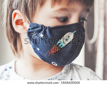 Boy with handmade protective mask on face. Fabric mask with embroidered space theme - comet, spaceship and stars. Stay home. Quarantine because of coronavirus COVID19. 