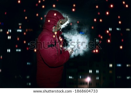 unrecognizable man using smartphone at night standing in dark space. steam from breathing. house building background. 