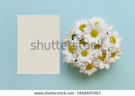 Greeting card mockup with daisies. Bright blue background with chamomile. Minimalism concept. Floral backdrop. Top view. Perfect for presentations, decor and web design.