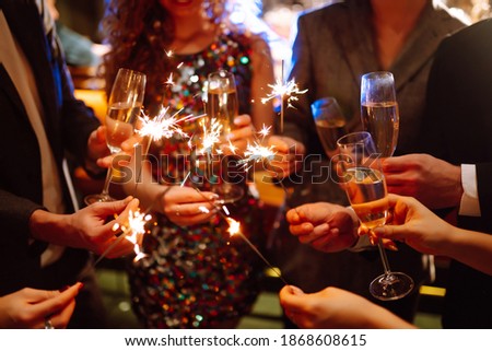 Glowing sparkles in hands. Group of happy people enjoying party with fireworks. Winter holiday, youth, lifestyle concept.