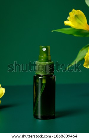 Clear spray bottle with flower on green background. Natural organic cosmetic packaging design.