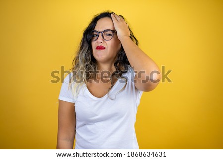 Young beautiful woman wearing casual white t-shirt over isolated yellow background putting one hand on her head smiling like she had forgotten something
