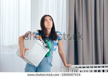 Tired Mother Holding a Basket of Dirty Laundry in Nursery Room. New mom feeling exhausted dealing with household chores
 Royalty-Free Stock Photo #1868687656