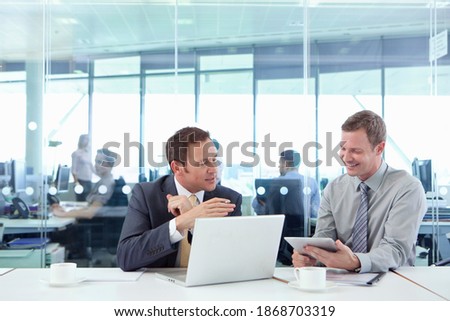 Two Businessmen using a laptop and a digital tablet while working in the conference room