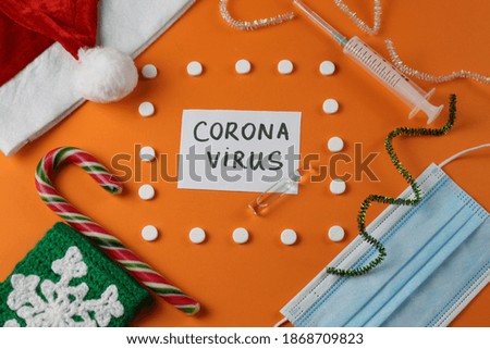 Composition from Santa hat, lollipop, face mask, ampoule, syringe. Lettering on a piece of paper: Coronavirus