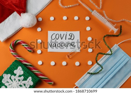 Composition from Santa hat, lollipop, face mask, ampoule, syringe. Lettering on a piece of paper: COVID vaccine