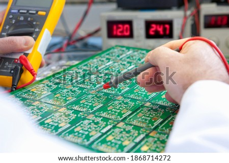 A closeup of a circuit board being checked by an engineer using a test head connected to the multimeter