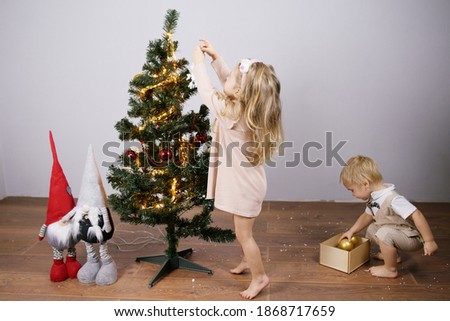 A small boy and girl ornaments on Christmas tree with light, baubles. Eve new year