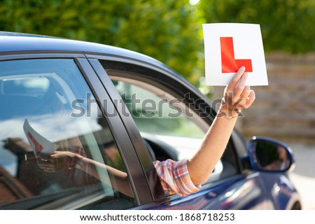 A medium shot of a woman's hand holding a learner's permit sticker out of a car window.