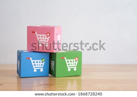 Color parcel carton box with shopping trolley cart logo on wooden table with white wall background. E-commerce or online shopping, logistic inventory control, cash on delivery (COD), wfh concept.