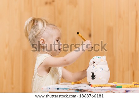 Little girl paints a piggy bank with markers