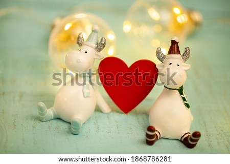 decorative bulls, symbol of 2021, on a sled with a decorative red heart on a turquoise wooden background close-up