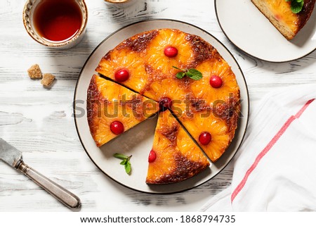 Homemade pineapple upside down pie with candied cranberry . Tropical dessert on white wooden background . Top view. Royalty-Free Stock Photo #1868794735