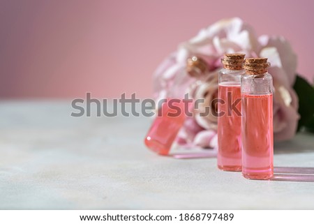 Perfumed Rose Water or essential oil in glass bottle and rose flower on a light background. Selective focus, copy space