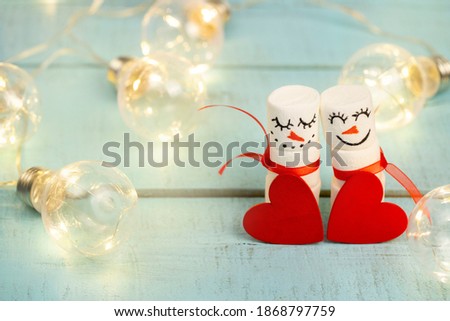 decorative marshmallow snowmen with a decorative red heart on a garlanded turquoise background close up