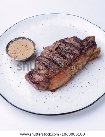 Delicious beef steak with sauce served on a white plate over white background. BBQ meat, barbecue concept. Tasty dinner idea.