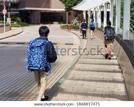 Chinese and Indian Boy and girls of international elementary- primary school carrying heavy big school bags  return home or go to school, walking along street in Hong Kong on sunny day Royalty-Free Stock Photo #1868817475