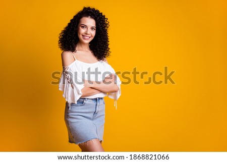 Photo of optimistic lovely brunette woman standing empty space crossed hands wear white top blue skirt isolated on yellow color background