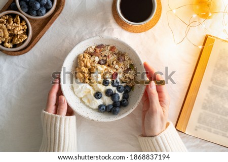 Top view book and Christmas healthy lifestyle breakfast with granola muesli and yogurt in bowl on white table backgroaund, cereal grain food with nuts seed. Organic morning diet meal 