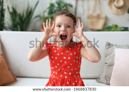 Adorable little girl making faces while sitting on sofa ta living room.