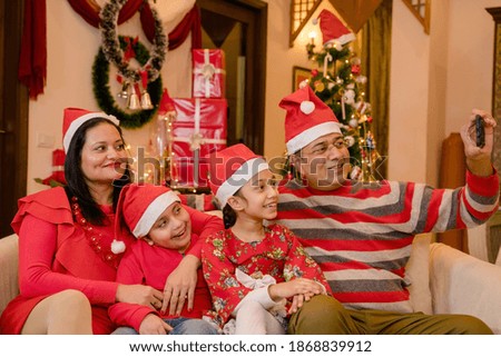 Family sitting on sofa at home wearing red caps taking selfie on Christmas day