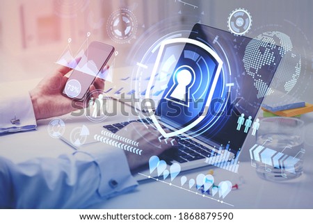 Hands of businessman using laptop and smartphone in blurry office with double exposure of cyber security interface. Toned image
