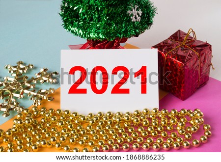 Christmas tree decorated with toys and tinsel, gift boxes and greeting card with text 2021. Can be used for congratulations