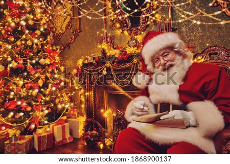 Santa Claus bagging Christmas presents, checking out a list of wishes. He sits in an armchair in a beautiful Christmas interior. Christmas and New Year concept. 