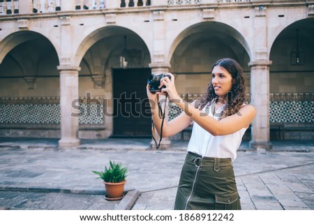Concentrated young woman in casual wear holding camera focusing on city architecture during vacations trip, serious beautiful female photography amateur using modern camera for learning outdoors