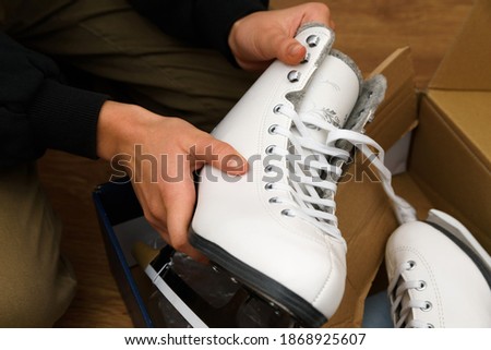 Young teenage girl sits on the wooden floor and unboxes a pair of brand new white figure skates, presented on the holiday