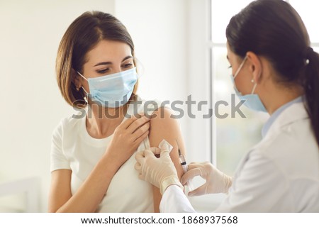 Vaccination, immunization campaign, disease prevention concept. Young woman in medical face mask getting Covid-19 vaccine at doctor's office. Professional nurse giving flu injection to patient Royalty-Free Stock Photo #1868937568