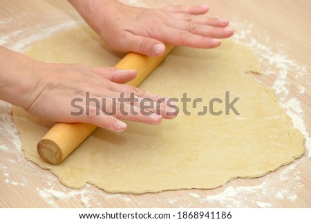 Women's hands roll out the dough with a rolling pin