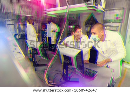 Young adult male and female colleagues in face masks trying to solve conundrum using computer to get out of escape room during corporate event. Toned image with glitch effect