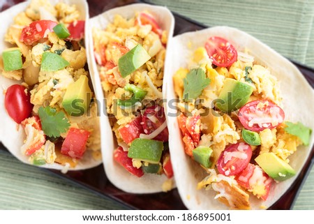 Tacos filled with migas, a Tex-Mex dish of eggs scrambled with red bell pepper, onions, jalapenos, cheese, topped with avocado, cilantro, cherry tomatoes